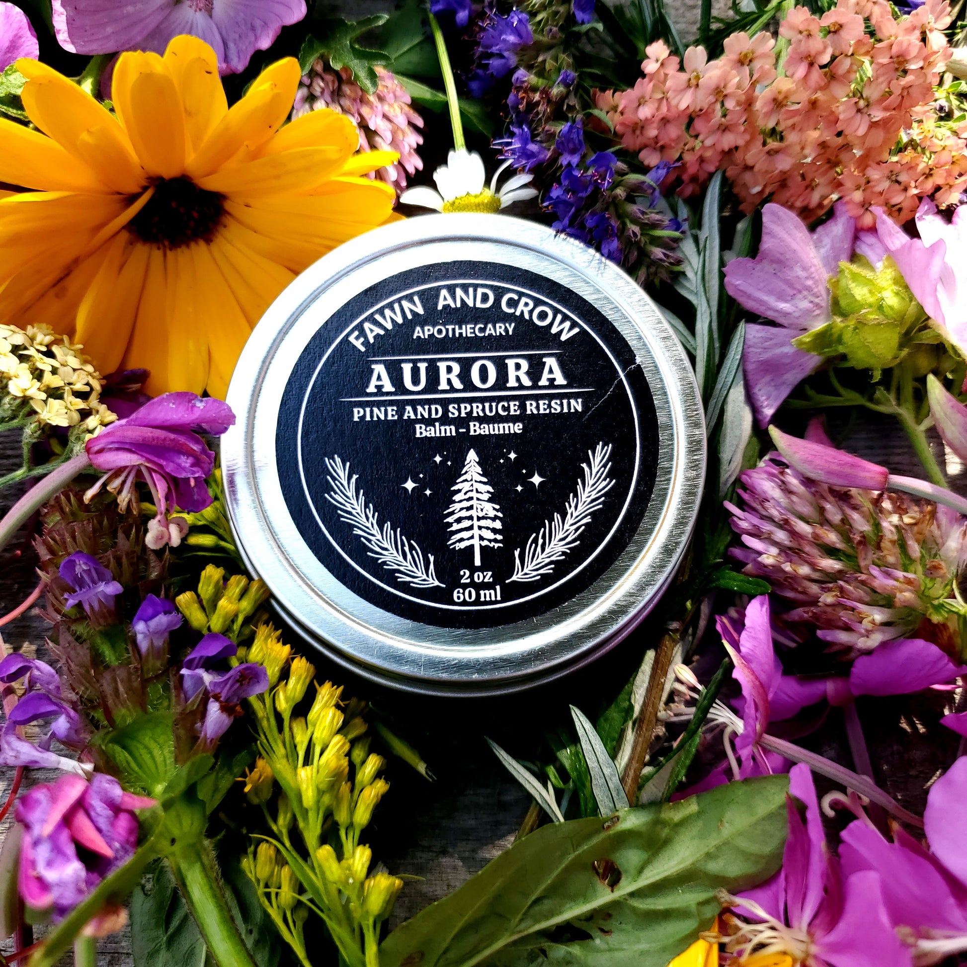 Balm balm container labeled 'Aurora' by Fawn and Crow Apothecary surrounded by colorful flowers.