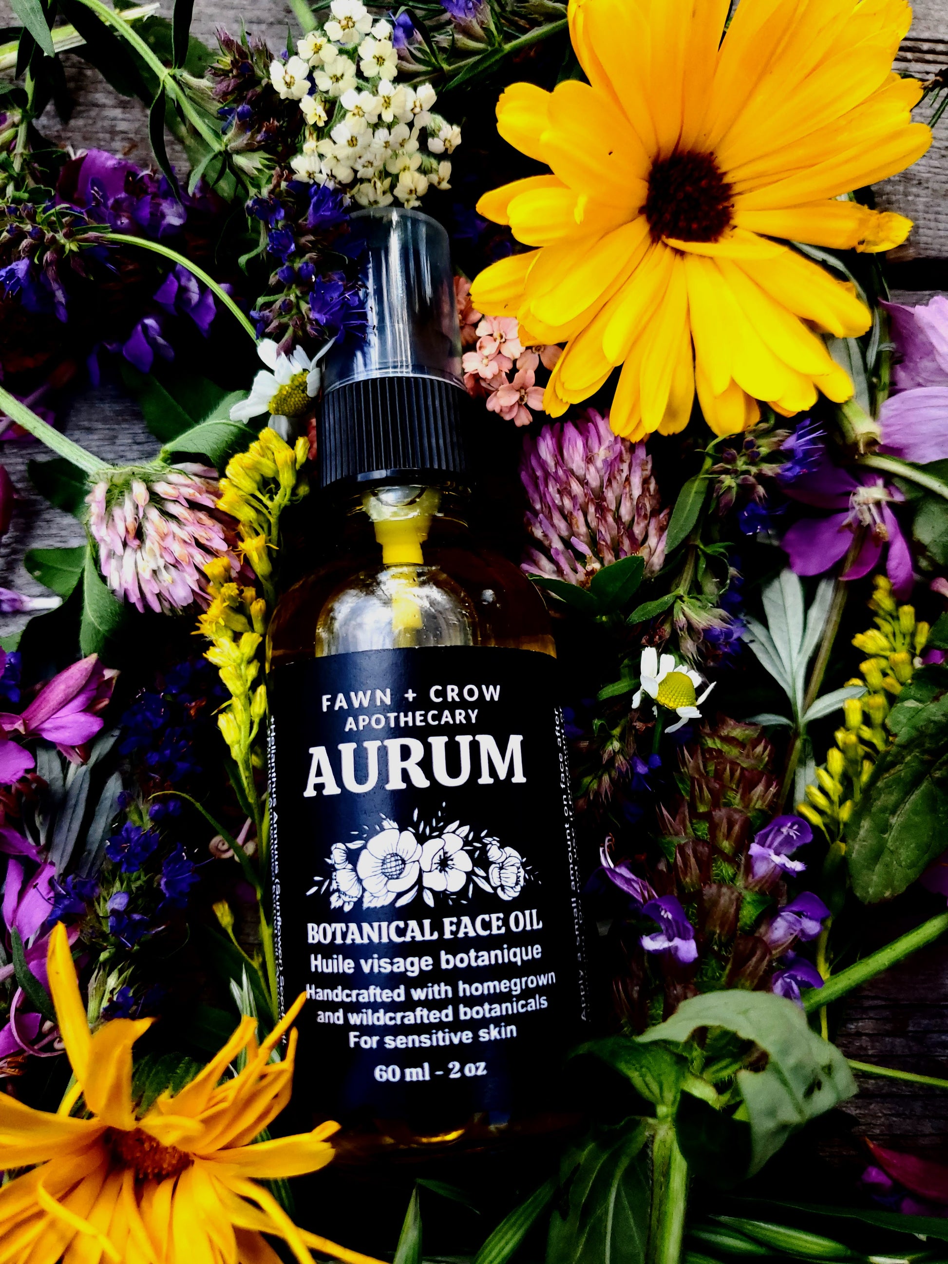 Bottle of Fawn + Crow Apothecary Aurum Botanical Face Oil surrounded by flowers on a wooden surface