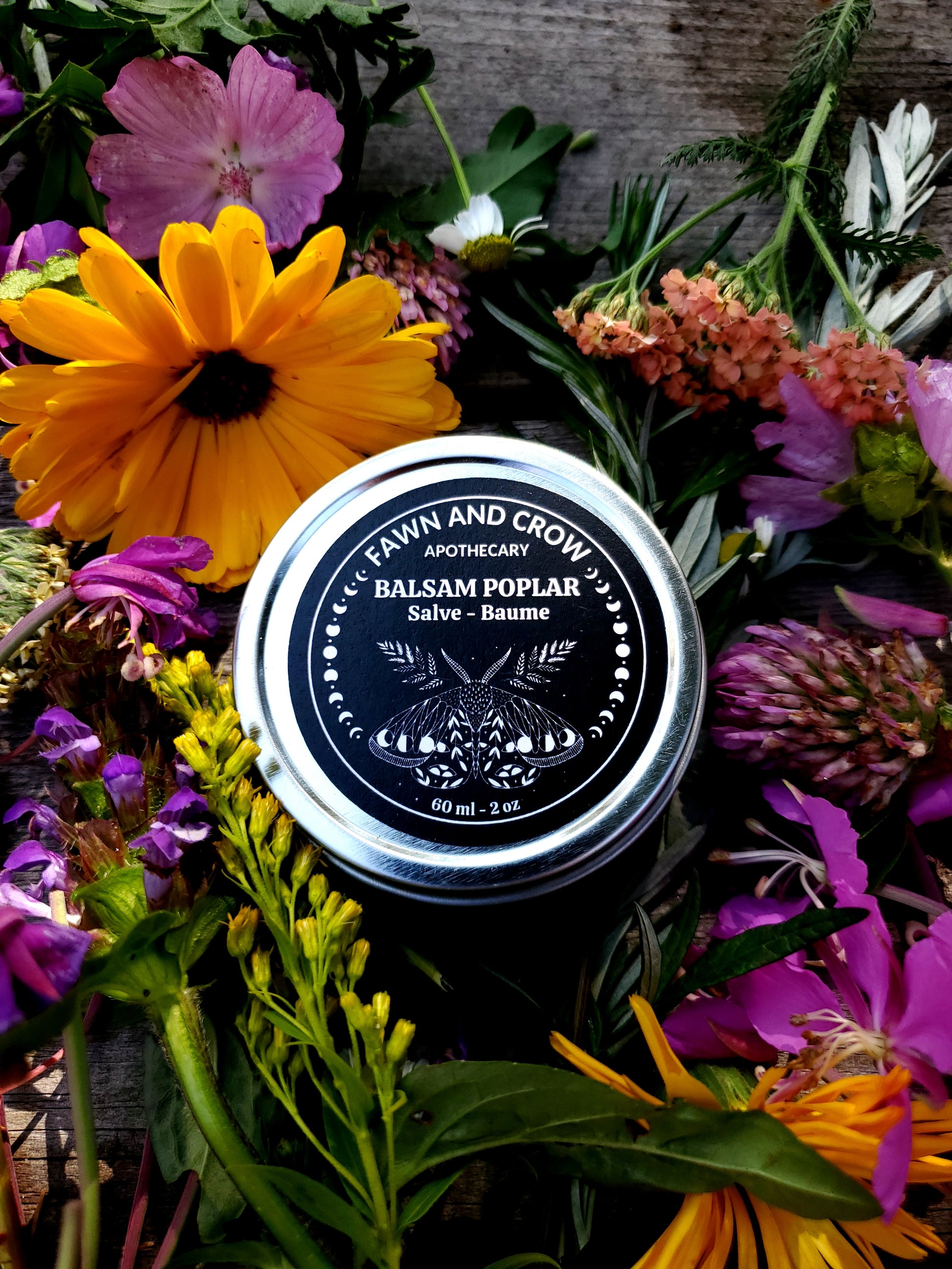 Balm jar surrounded by colorful flowers on a wooden surface