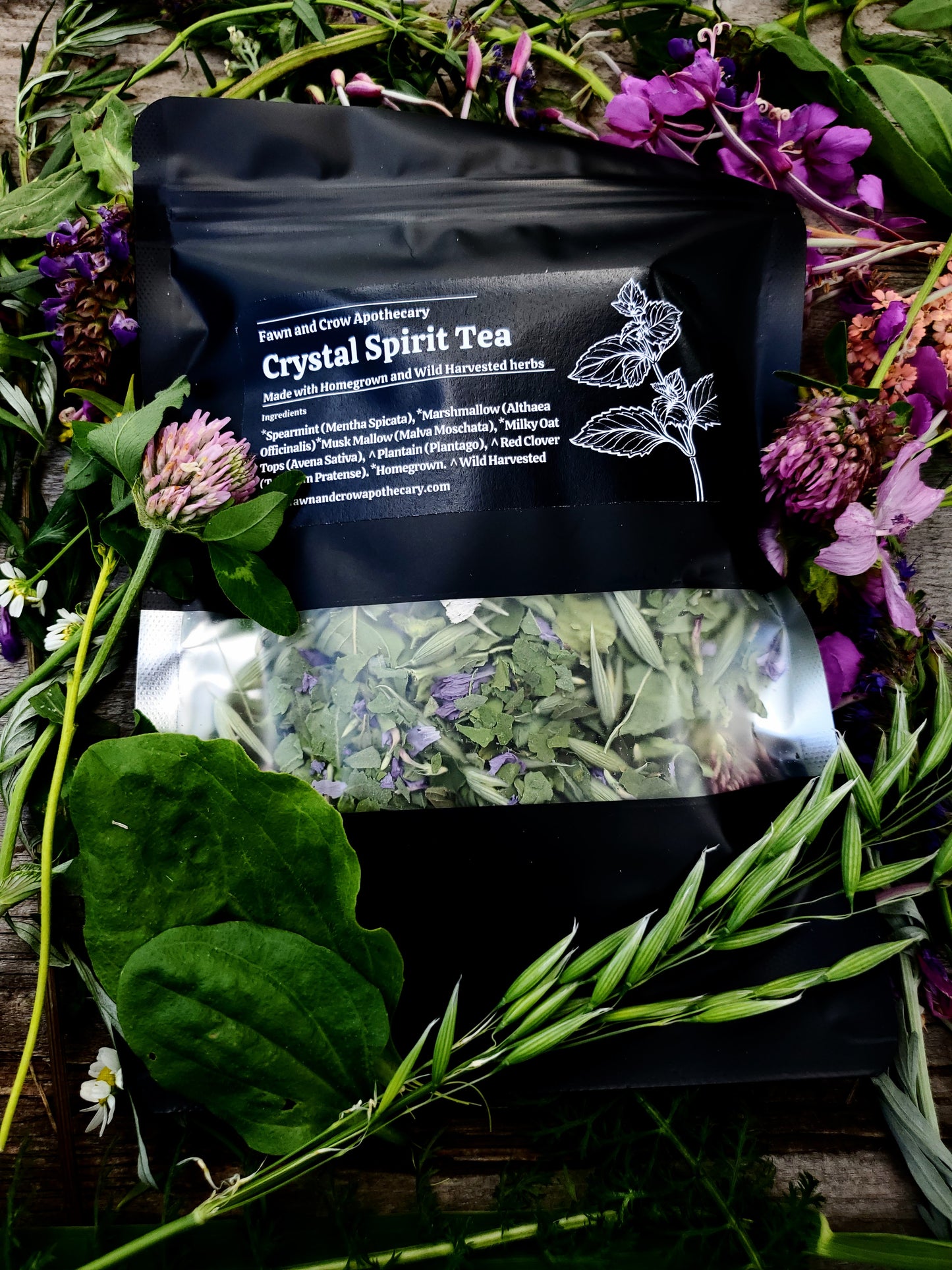 Crystal Spirit Tea package surrounded by herbs and flowers on a wooden surface