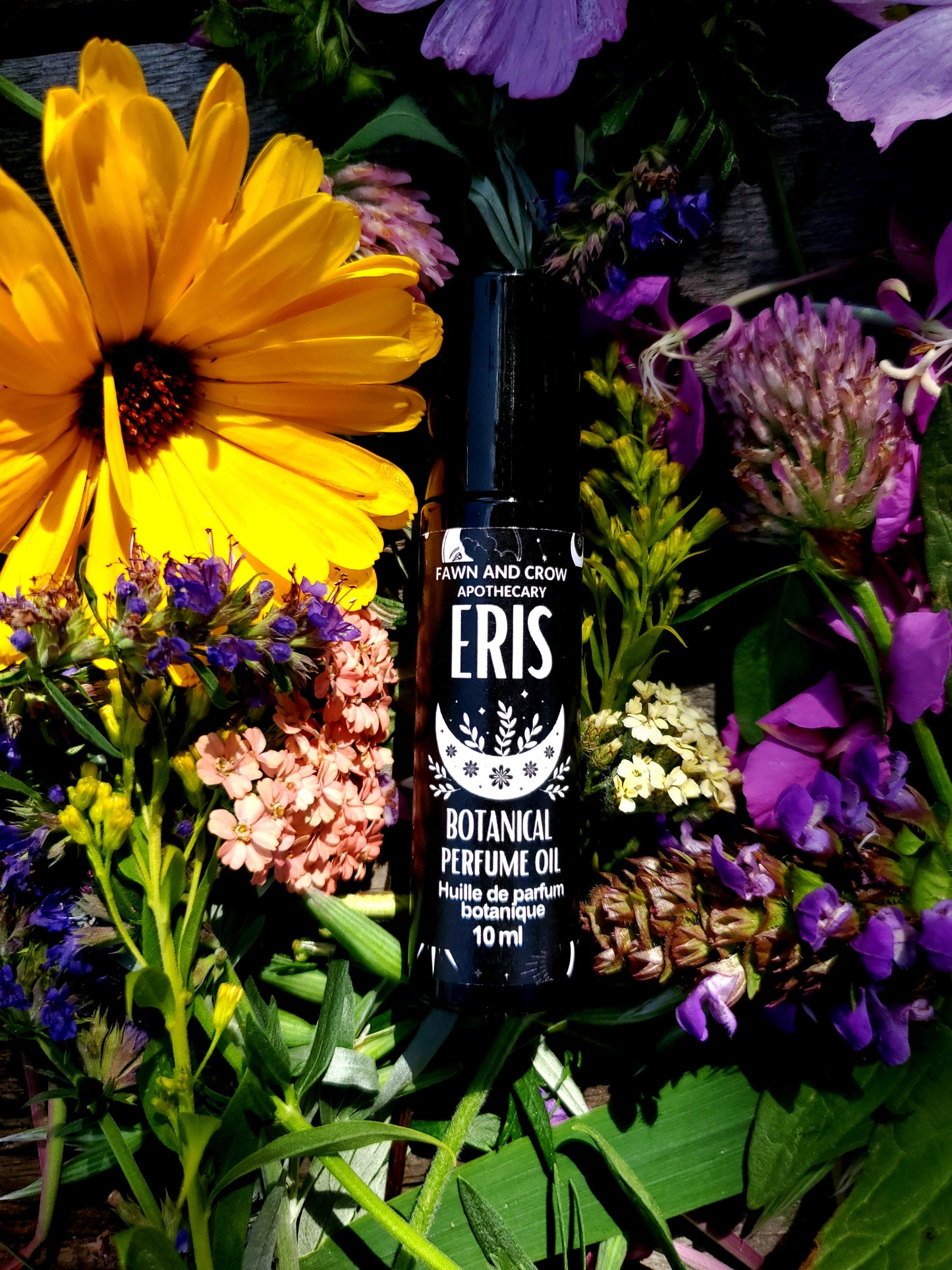 Eris Botanicals perfume oil bottle surrounded by a variety of flowers and greenery