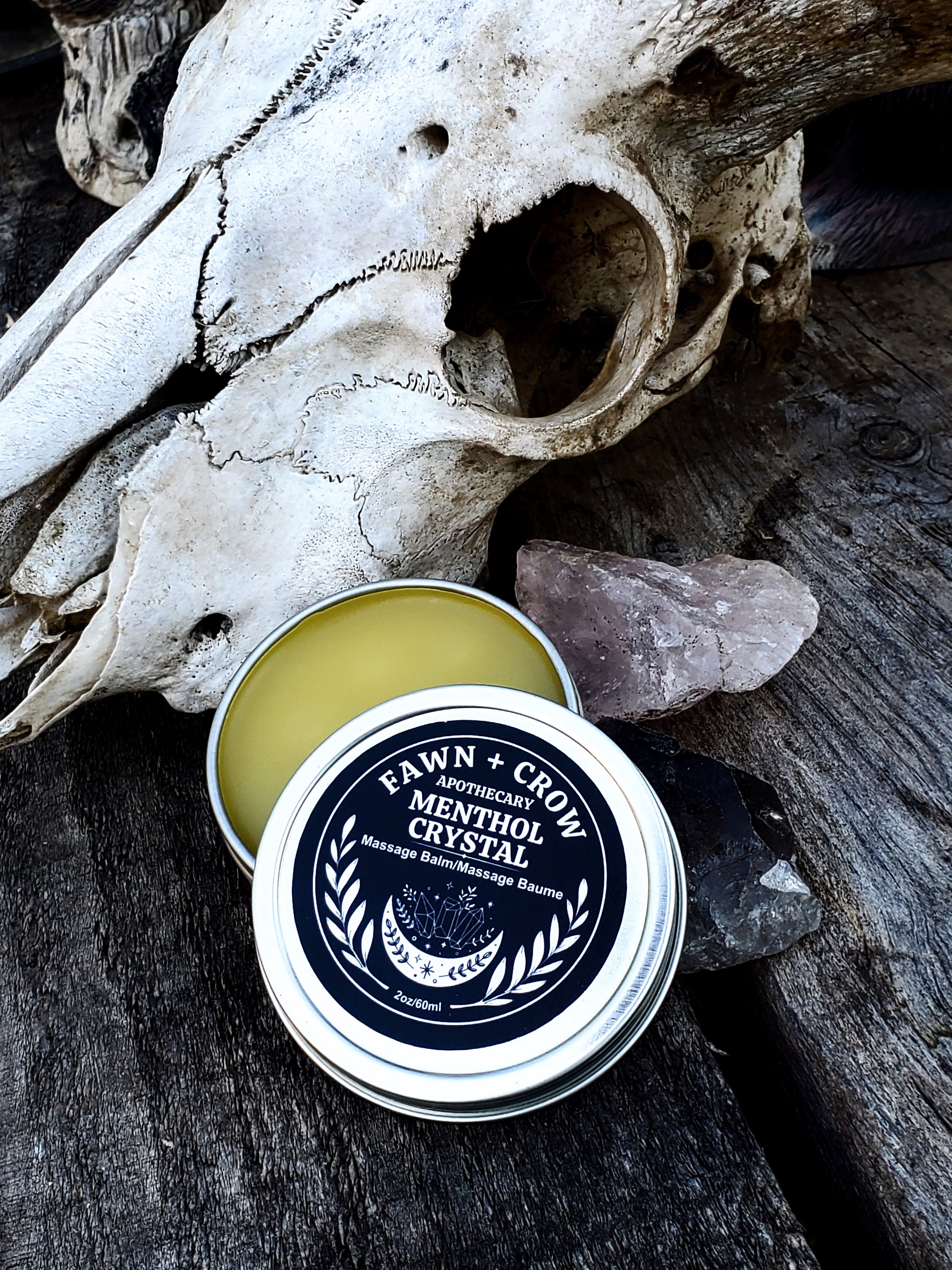 Tin of Fawn + Crow balm on a wooden surface with a skull in the background