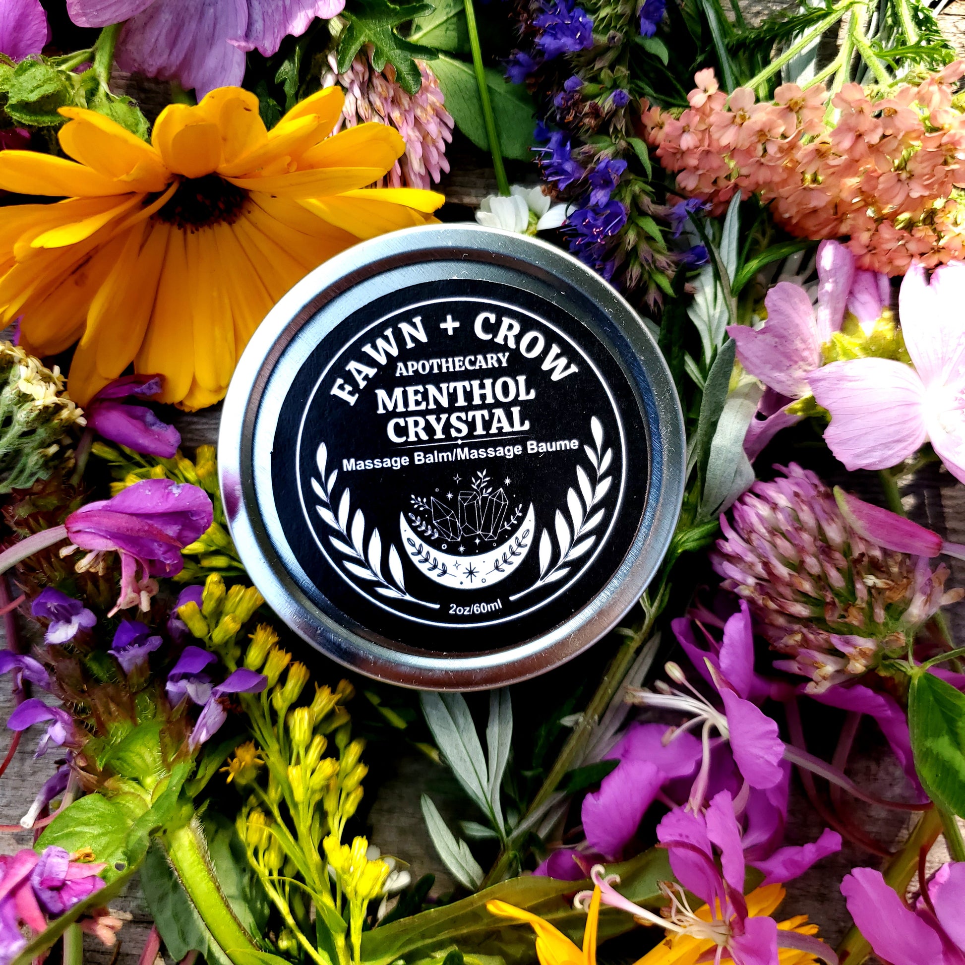 Tin of 'Fawn and Crow Menthol Crystal massage balm surrounded by a colorful array of flowers