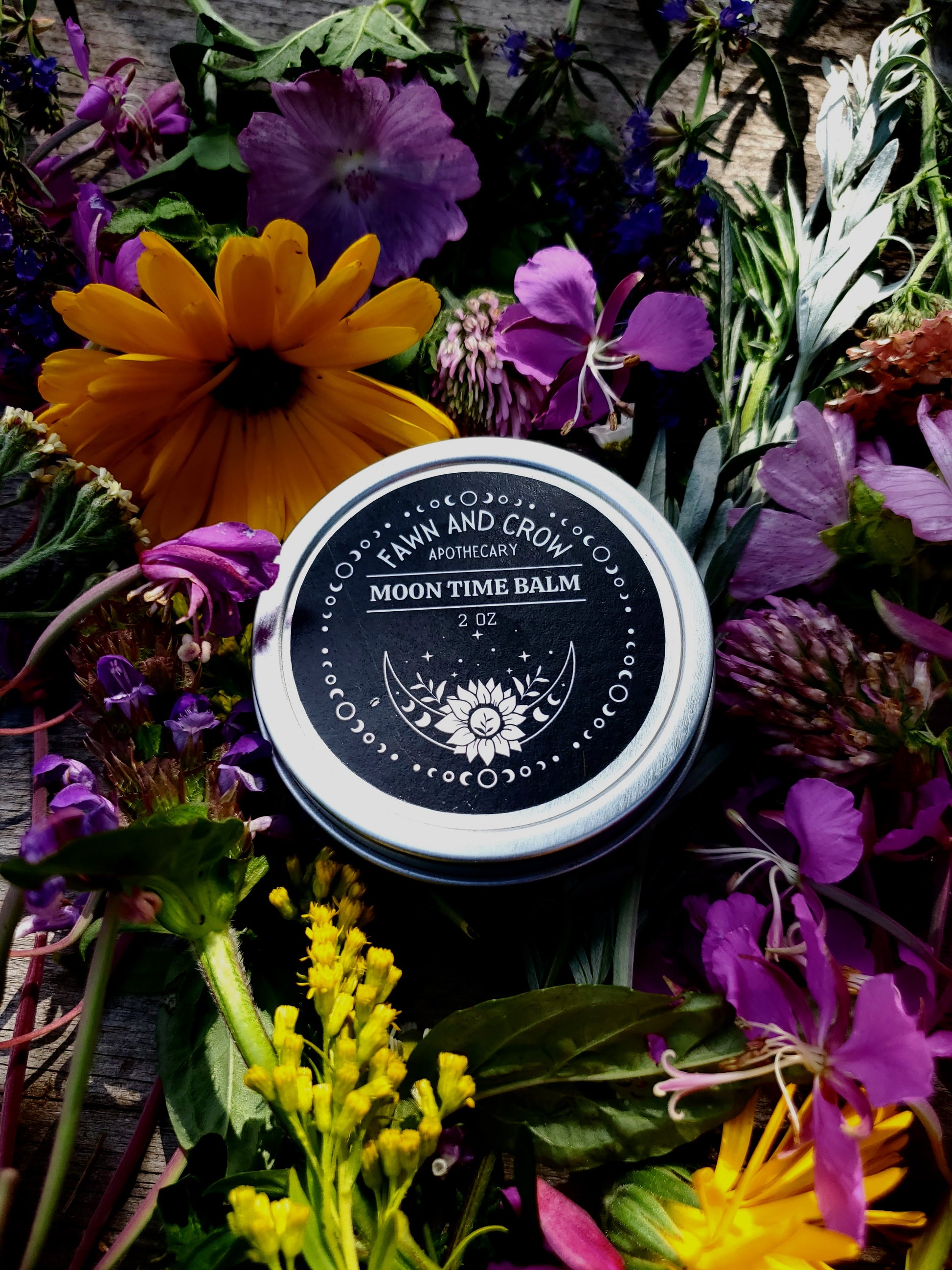 Moon Time Balm jar surrounded by colorful flowers on a wooden surface
