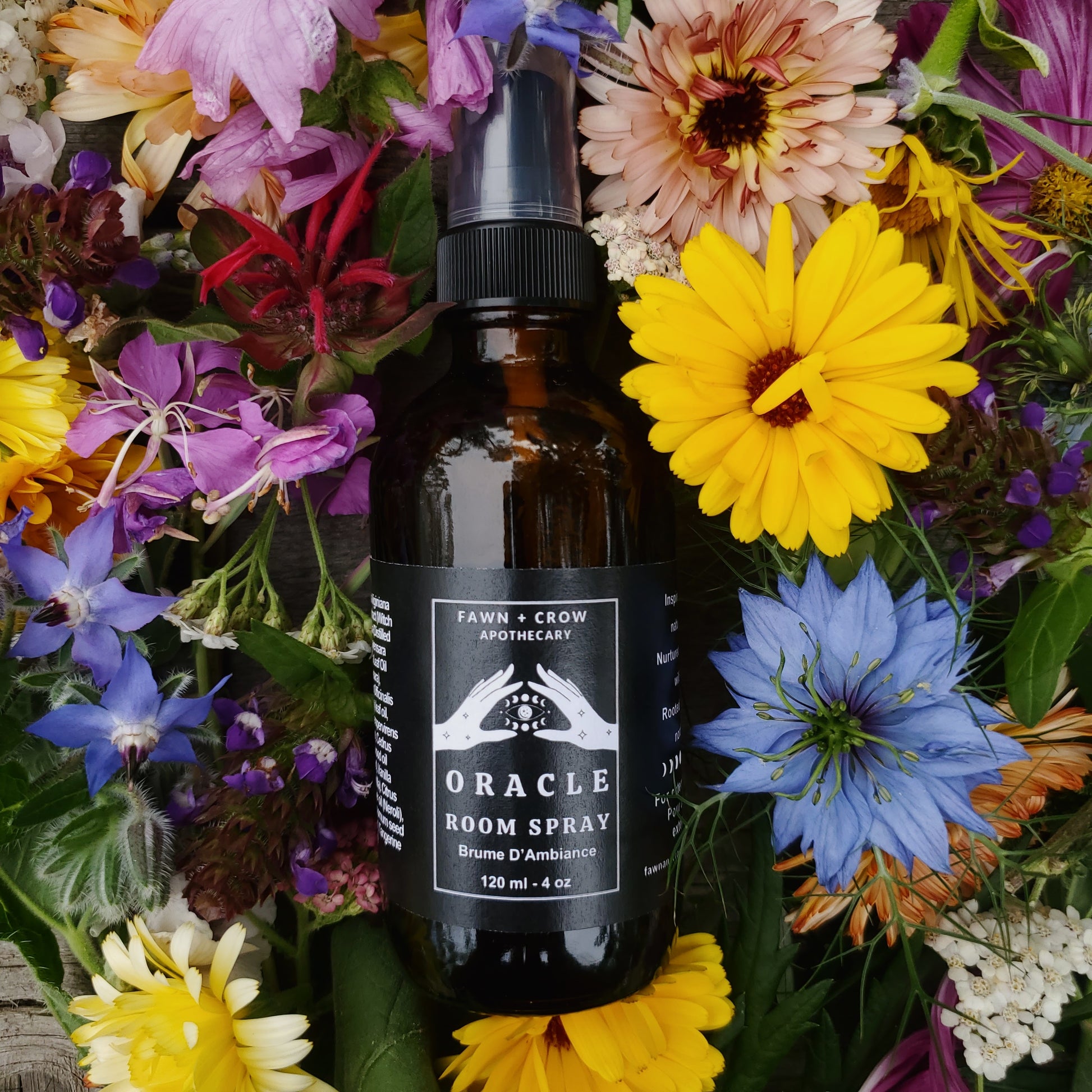 Oracle room spray in an amber bottle by Fawn and Crow Apothecary syrrounded by colorful flowers