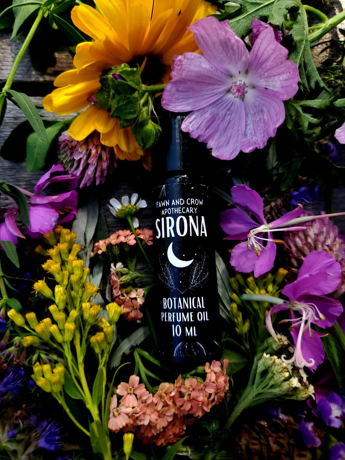 Sirona perfume oil bottle surrounded by colorful flowers on a wooden surface