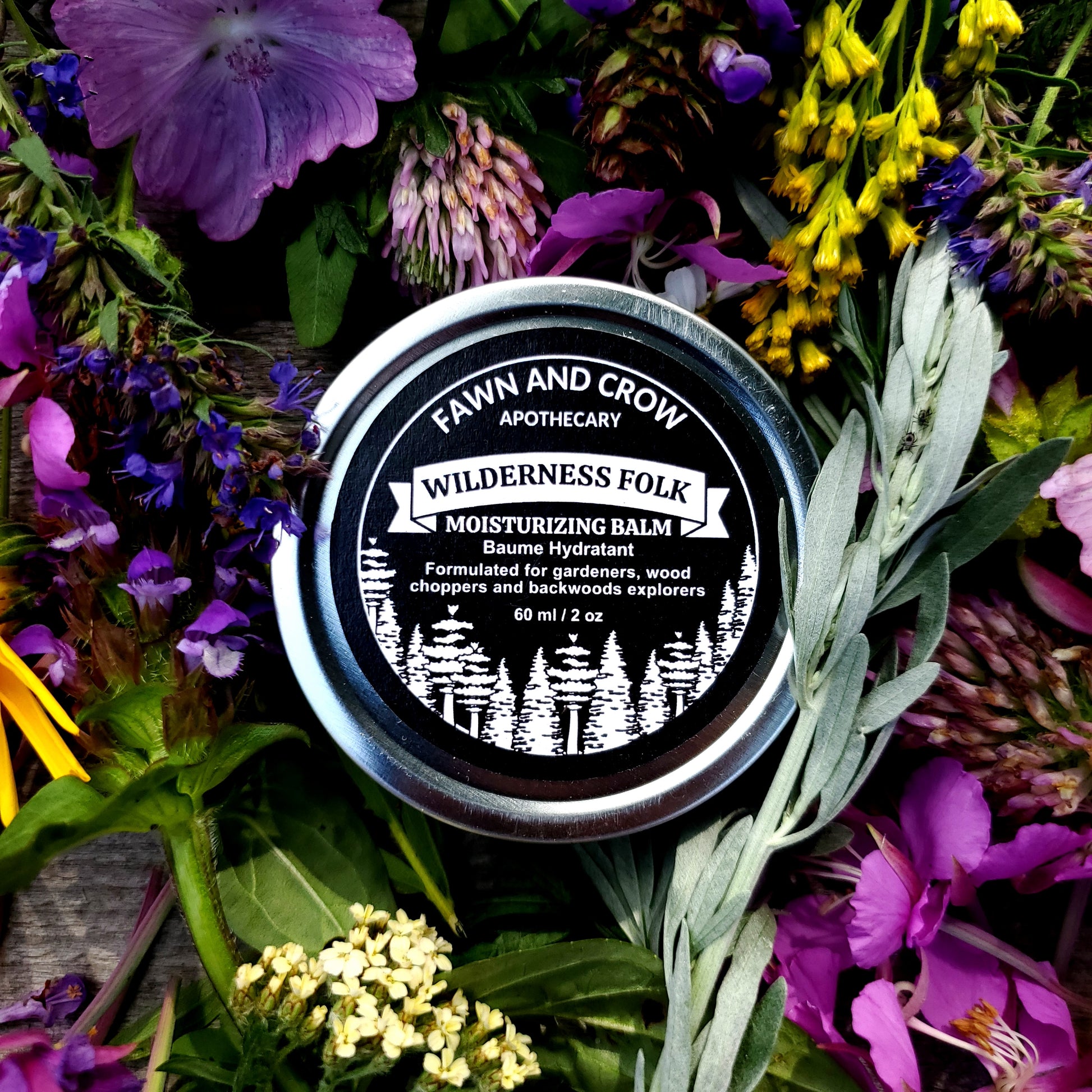 Balm container labeled 'Wilderness Folk' surrounded by wildflowers and greenery