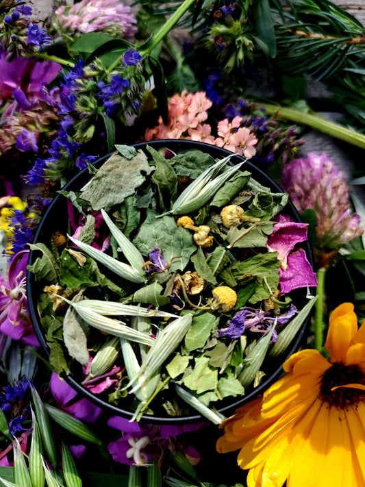 Herbal mix in a black tin surrounded by colorful flowers