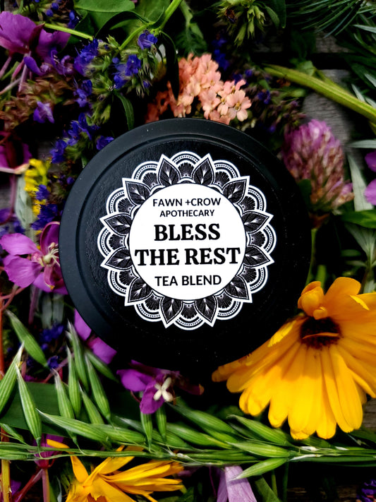 Tea blend container labeled 'Bless the Rest' surrounded by flowers and greenery