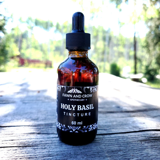 Bottle of Fawn and Crow Holy Basil Tincture on a wooden surface with blurred greenery in the background