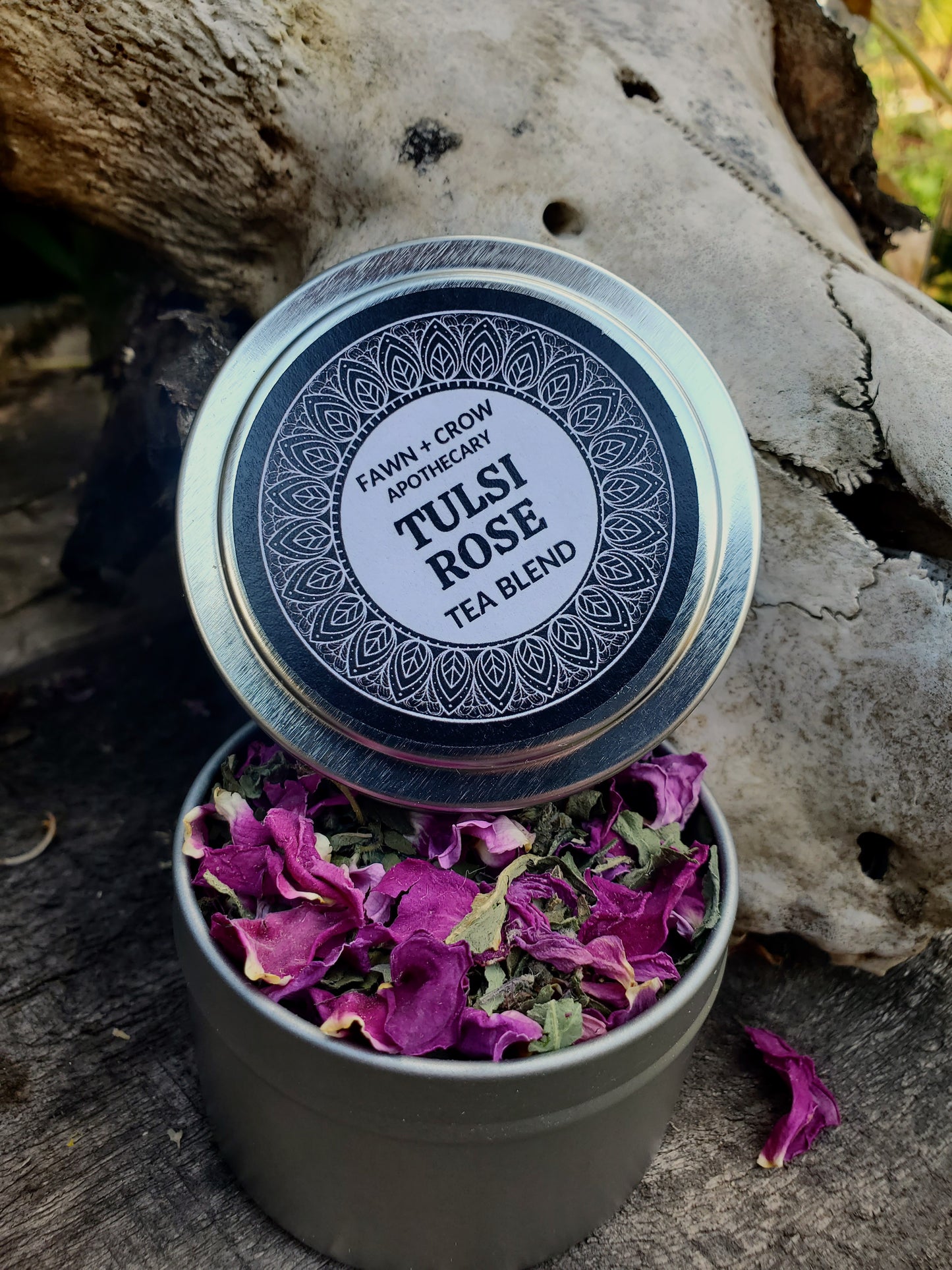 Tulsi Rose tea blend in a tin container with a decorative lid on a wooden surface.