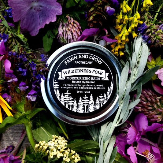 Balm container labeled 'Wilderness Folk' surrounded by wildflowers and greenery